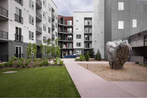 A large rock sits in the middle of a gravel area in front of a building.