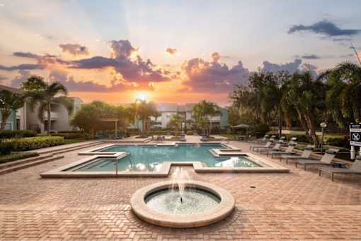 A sunset view of a pool with a fountain in the middle.