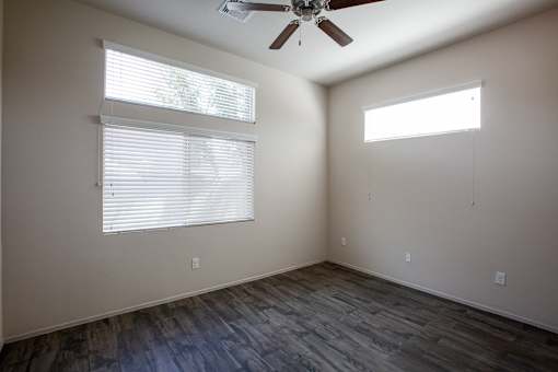 A room with a ceiling fan and two windows.