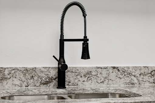 A black kitchen faucet with a pull-down sprayer is installed over a sink.