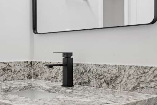 A black faucet with a sink and a mirror above it.