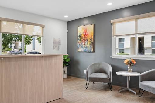 A reception area with a wooden desk, two chairs, and a painting on the wall.