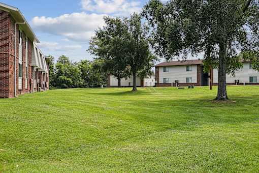 A grassy field with trees and apartment buildings in the background.