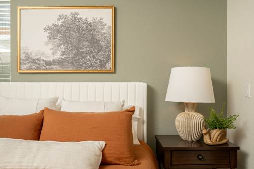 A bedroom with a bed, nightstand, lamp, and a picture on the wall.