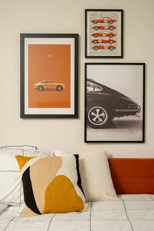 Three framed pictures of cars are hanging on a wall above a bed with a white comforter and two pillows.