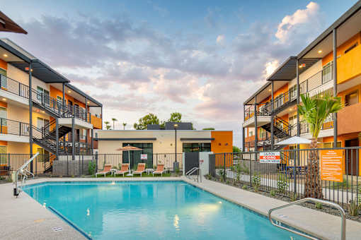 A swimming pool is surrounded by a fence and chairs in front of a building.