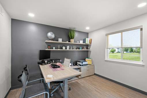 A room with a desk, chair, and shelves with various items.