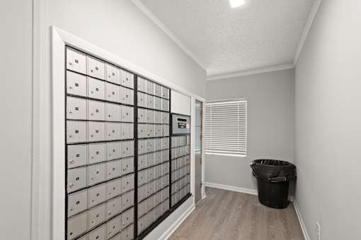 A room with a wall of mailboxes and a trash can.