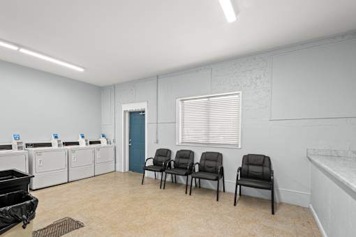 A room with a row of chairs and a row of washing machines.