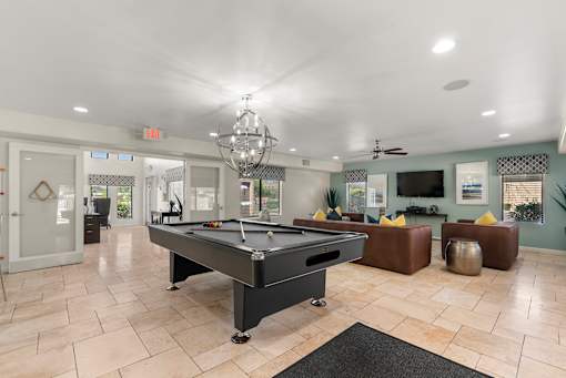A pool table is in the middle of a room with a chandelier hanging from the ceiling.