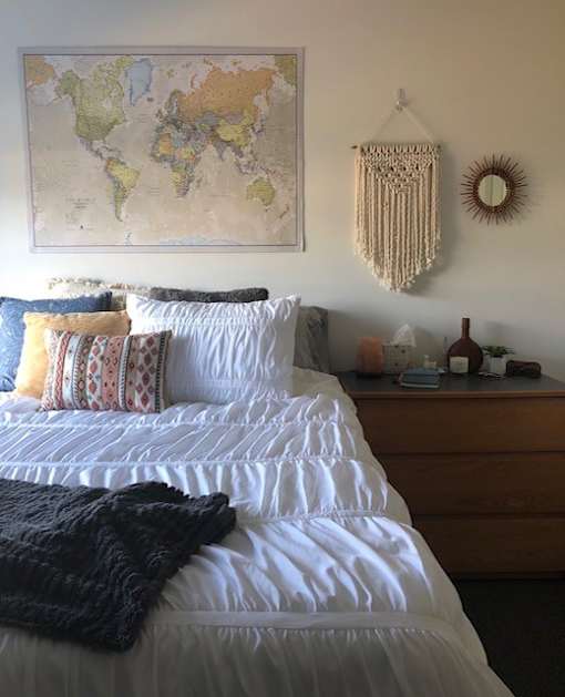 A bedroom with a world map on the wall and a bed with white sheets and a black throw.