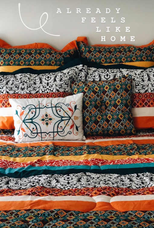 A bed with a colorful comforter and pillows with the text "ALREADY FEELS LIKE HOME" overlaid.