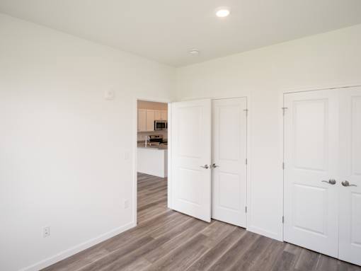 A room with white walls and wooden floors with three white doors.