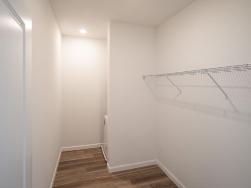 A white wall with a shelf and a wooden floor.