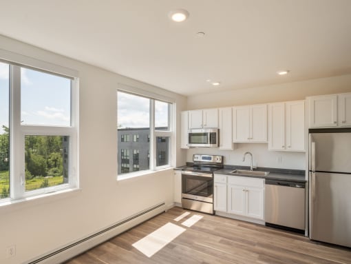 a kitchen with white cabinets and stainless steel appliances and large windows