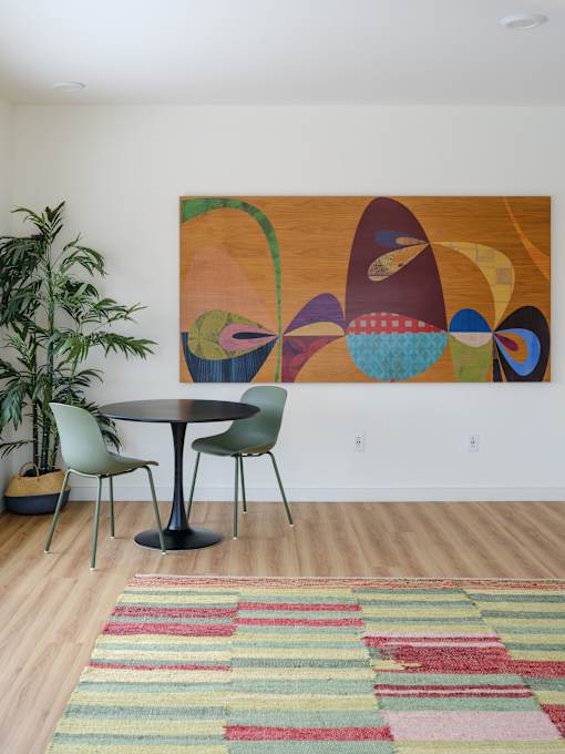 A large abstract painting hangs on a white wall above a round table with four chairs.