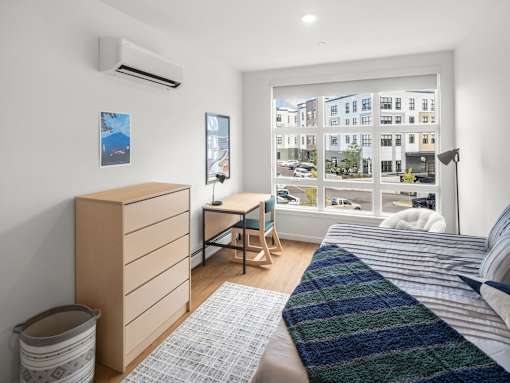 A bedroom with a bed, desk, and window overlooking a street.