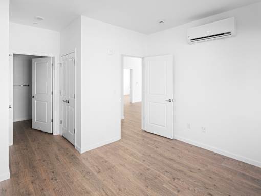 A room with white walls and wooden flooring, featuring a white door and a white cabinet.