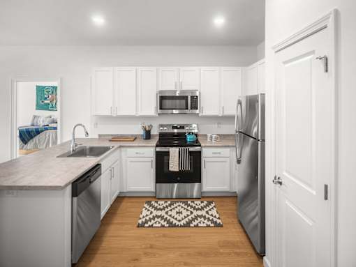 A kitchen with white cabinets and a black and white rug on the floor.