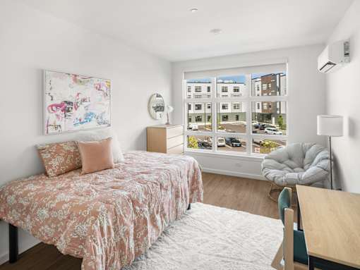 A bedroom with a bed, chair, and a window with a view of buildings outside.