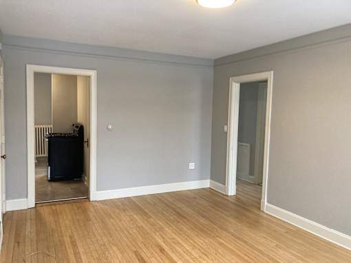 A room with light grey walls and wooden flooring with a white door and a mirror.