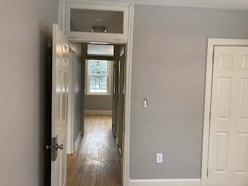 A hallway with a white door on the right and a window in the distance.