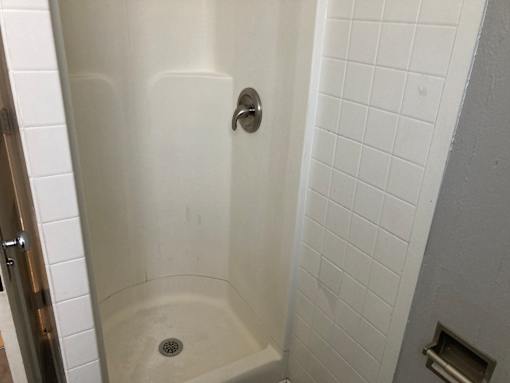 A white tiled shower stall with a drain in the middle.