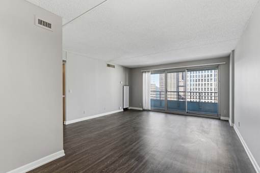 A room with a wooden floor and a view of a cityscape through the windows.