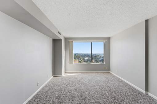 A room with a carpeted floor and a window overlooking a cityscape.