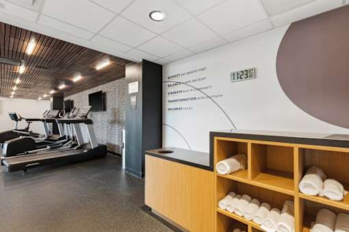 A gym with a treadmill, weights and a wall with a sign.