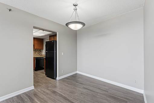 A room with a black refrigerator and wooden flooring.