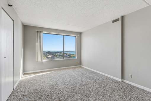 A room with a carpeted floor and a window overlooking a cityscape.