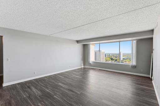 A spacious room with wooden flooring and a large window overlooking a cityscape.
