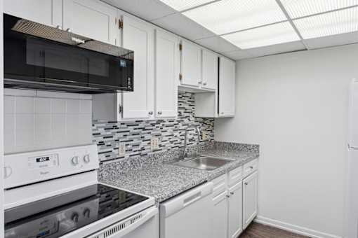 A kitchen with white cabinets and a black microwave.