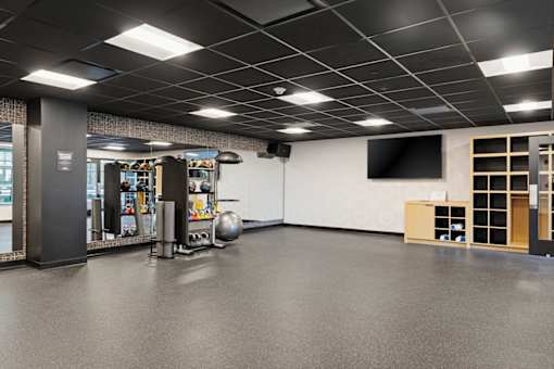 A gym with a grey floor and a white wall with a television.