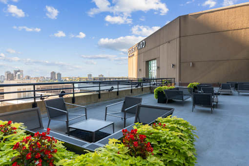 A rooftop patio with chairs and tables overlooking a city skyline.