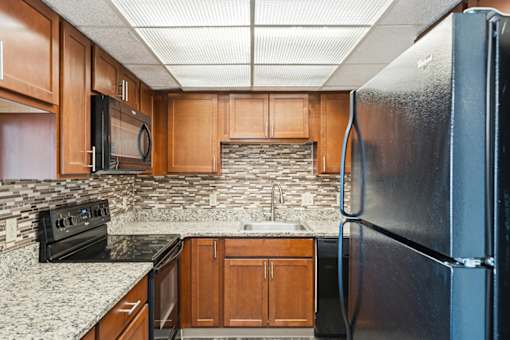 A kitchen with a black refrigerator and wooden cabinets.