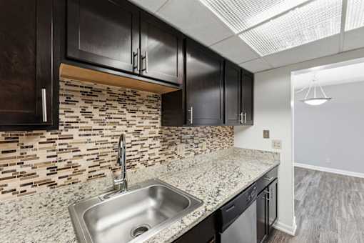 A kitchen with a stone backsplash and dark cabinets.