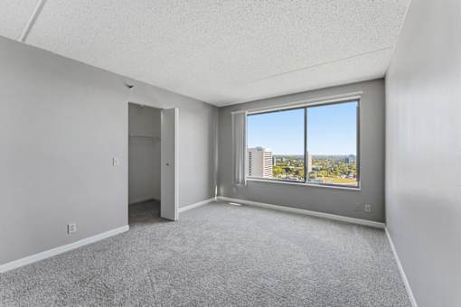 A room with a carpeted floor and a large window overlooking a cityscape.