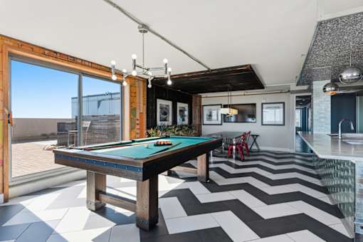 A pool table is in the middle of a room with a chevron patterned floor.