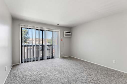 A room with a grey carpet and a sliding glass door leading to a balcony.