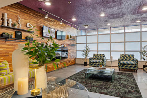 A living room with a wooden wall and a glass table with a candle on it.