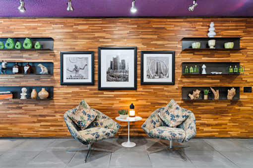 Two chairs and a table are in front of a wooden wall with pictures and shelves.