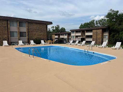 A swimming pool surrounded by sun loungers and apartment buildings.