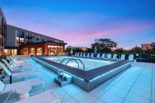 a pool with chairs and a building at dusk