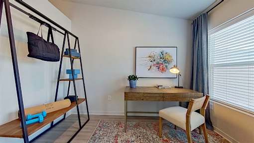 A sunlit room with an office desk, chair, shelving, and a large window.