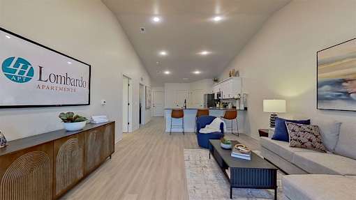 A spacious living room with light wood-style flooring and recessed lights in a vaulted ceiling.