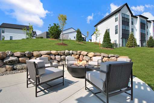 Two chairs are on a patio with a stone wall and a fire pit.