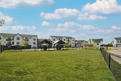 A grassy field with a fence and houses in the background.