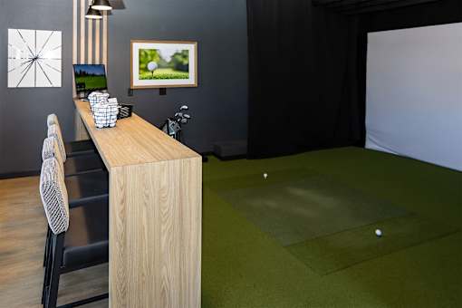 A room with a wooden desk and a golf ball on the green carpet.
